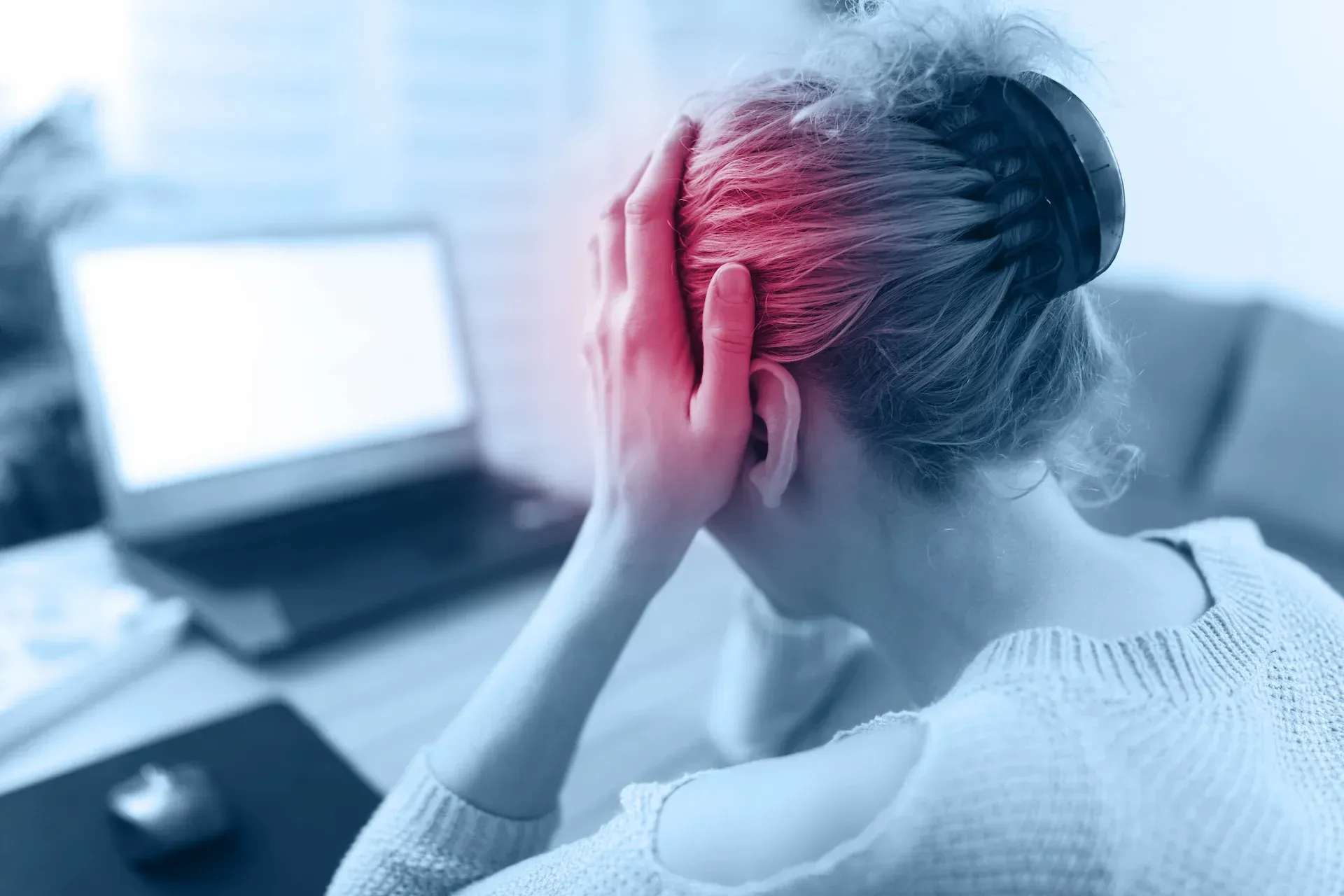 Woman at a laptop holding her head in pain