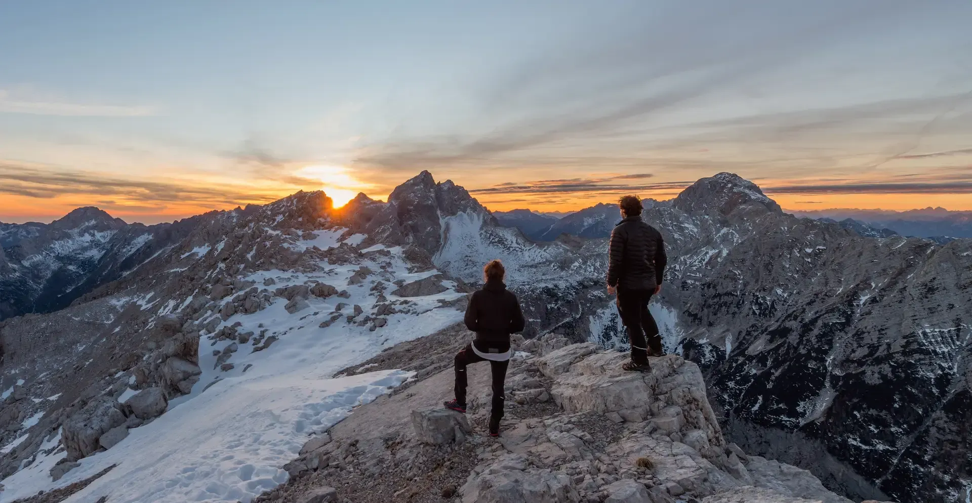 Two hikers watching sunrise over mountain peaks